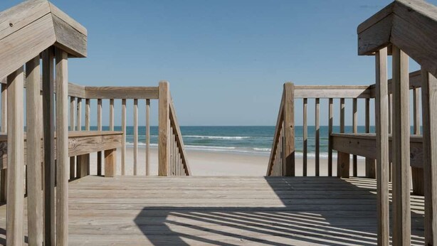 Une promenade en bois qui mène à une plage d’où l’on a une vue dégagée sur l’océan.