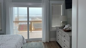 Une chambre à coucher comprenant un lit, une commode, une fenêtre avec des stores et donnant sur un balcon.