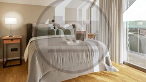 Un dormitorio moderno con una cama grande, una mesita de noche con una lámpara y vistas al exterior a través de cortinas translúcidas.