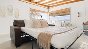 Ein modernes Schlafzimmer mit Bett, Sofa und Schreibtisch. Große Fenster bieten einen Blick ins Freie.