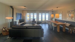 Una sala de estar moderna con sofá, televisor y comedor con vista al mar.