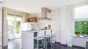 Una cocina moderna con una isla central, taburetes de bar, horno empotrado y ventana con vistas a zonas verdes.