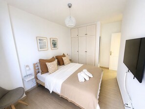 Un dormitorio con cama, televisión, armario y escritorio con lámpara.