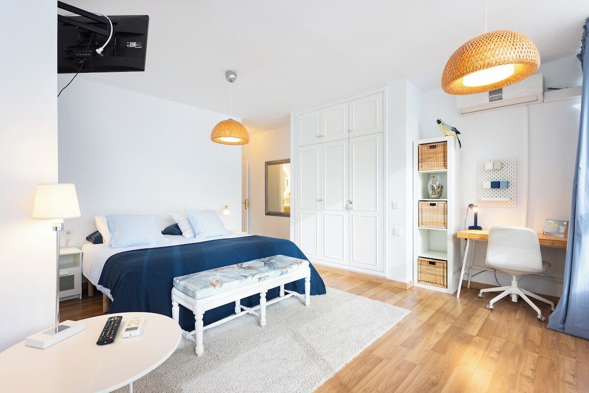 Habitación de hotel con cama, mesita de noche, lámpara, banco, escritorio, silla, armario y estanterías.