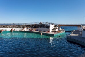 A swimming pool area with a stone wall, a bridge, and a clear blue sky. - Home2Book Lighthouse Apt Stunning Sea View Tabaiba (Tabaiba)