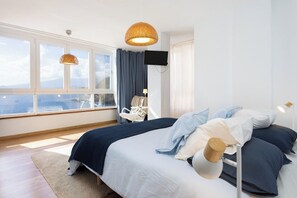 Une chambre avec un grand lit, une télévision et une vue sur la mer par les fenêtres.