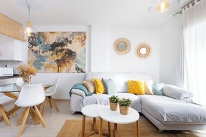 A modern living room with a sofa, a dining table with chairs, and a kitchen area.