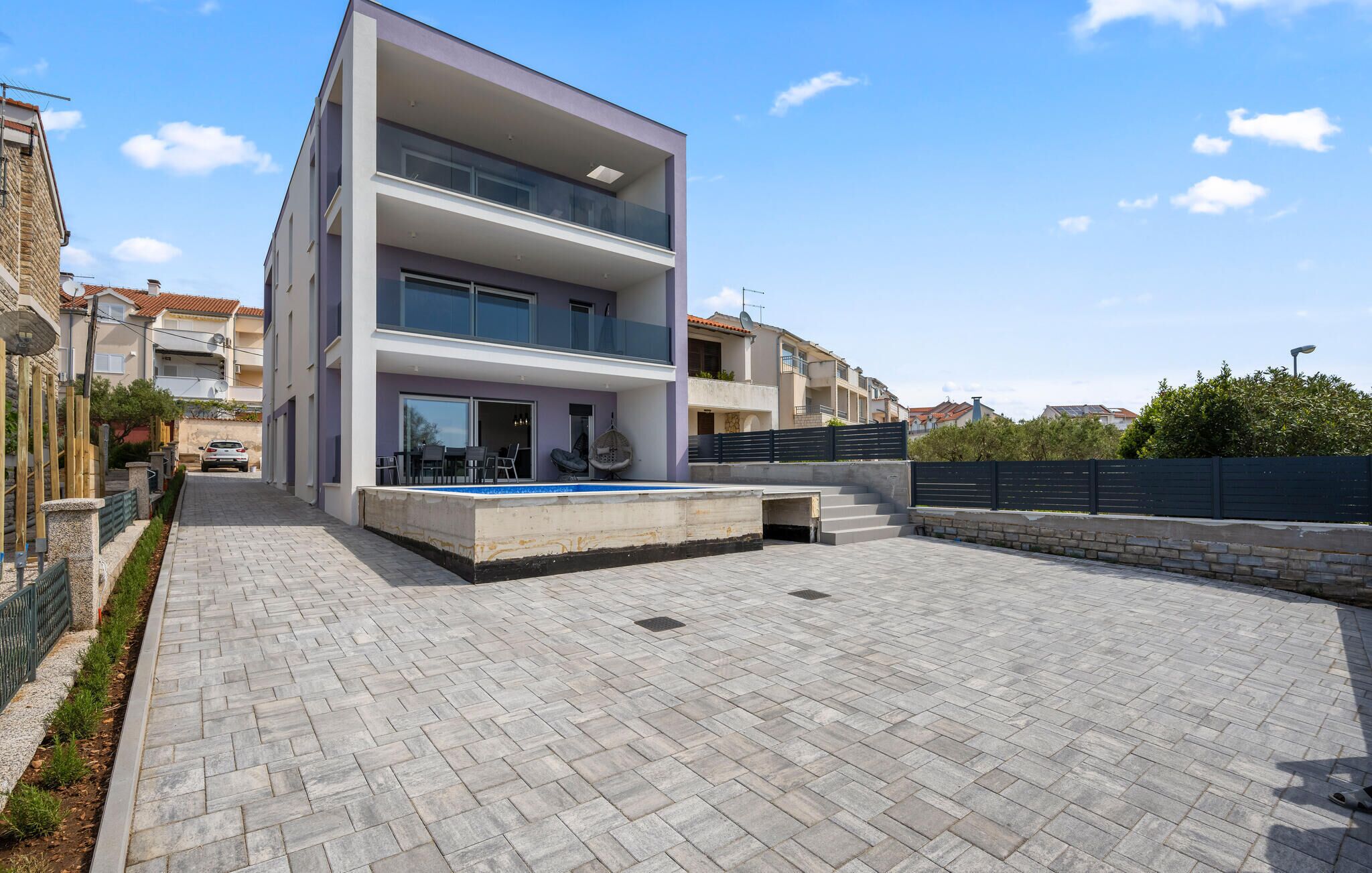 A modern two-story building with a flat roof, large windows, and a paved courtyard.