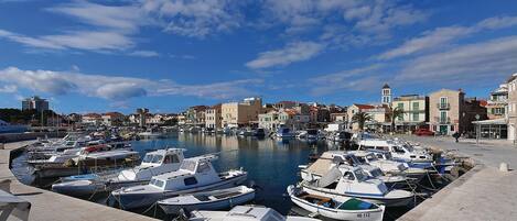 A marina with various boats docked, a clear sky, and buildings in the background.