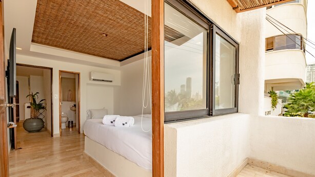 A modern bedroom with a large window, a bed, and a view of the city. - Casa Griega By Wynwood House (Cartagena)