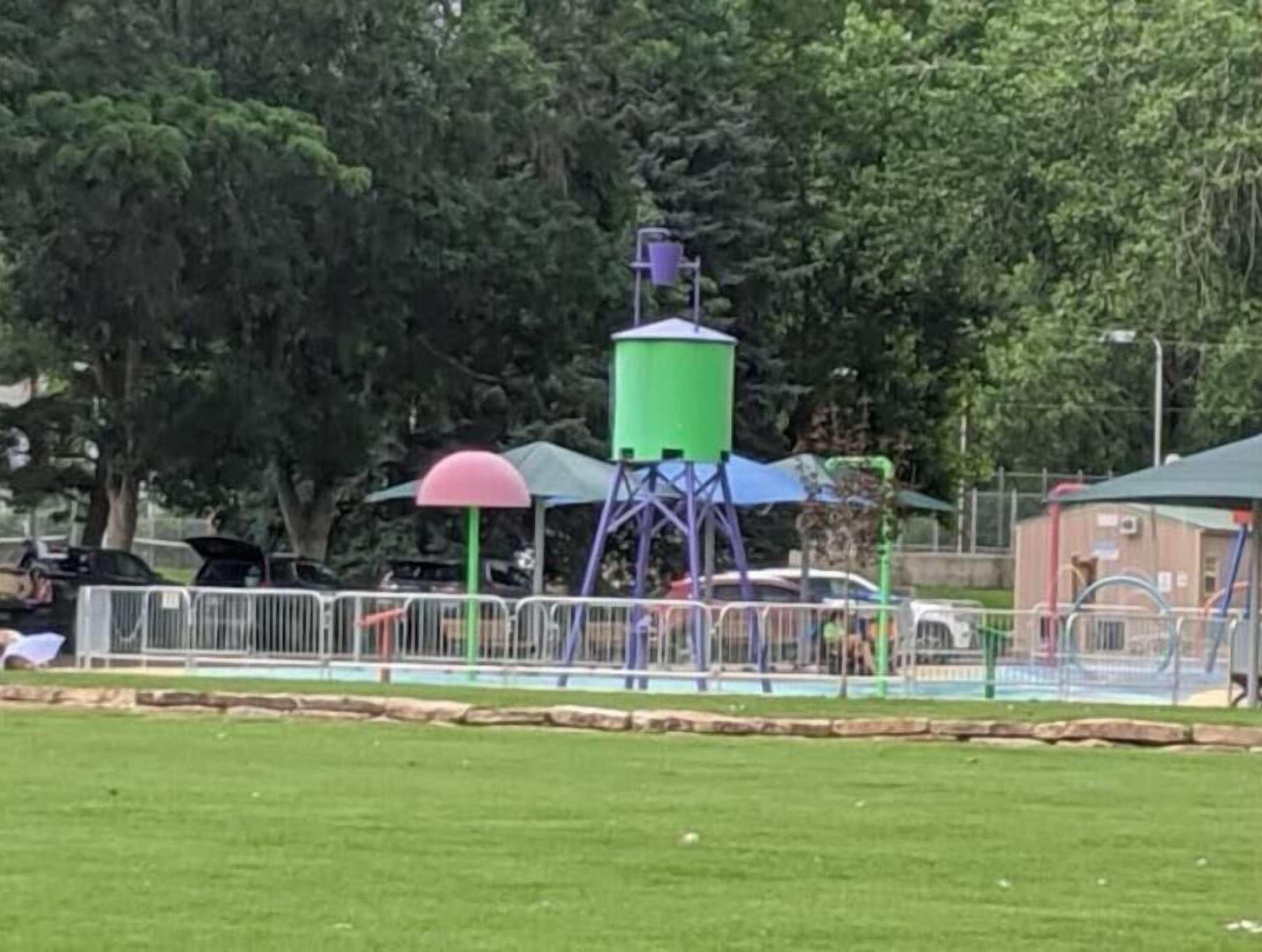 Ein Spielplatz mit bunten Spielgeräten, darunter ein Wasserturm und ein eingezäunter Bereich.