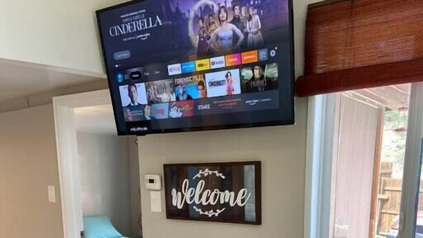 Un comedor con una mesa y sillas de madera, un televisor de pantalla plana en la pared y un letrero que dice 'Welcome'.
