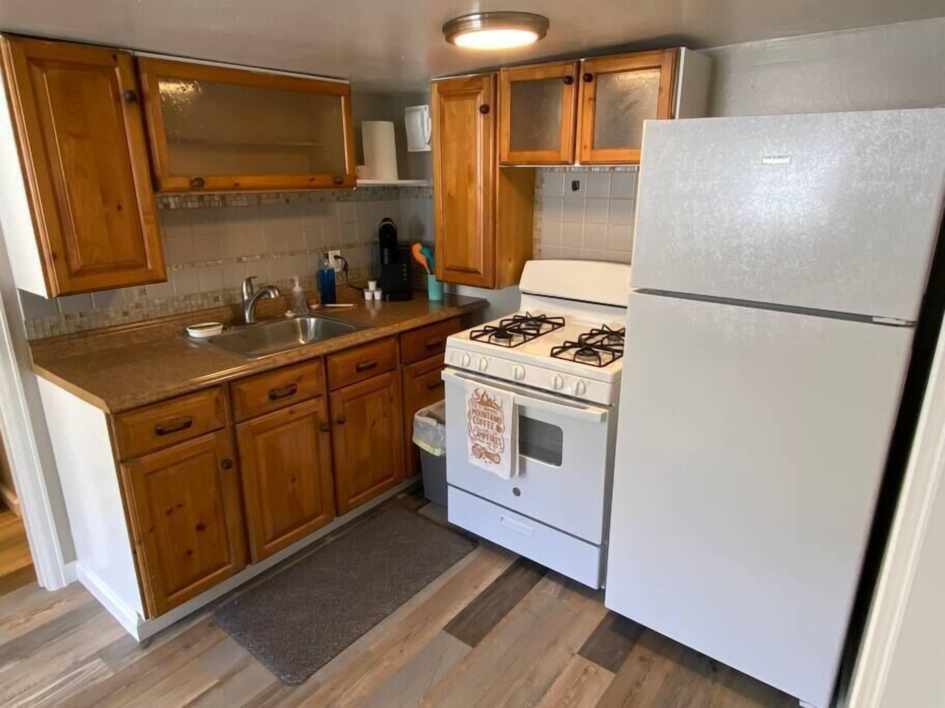 Une cuisine avec des meubles de rangement en bois, une cuisinière à gaz, un réfrigérateur et un évier.