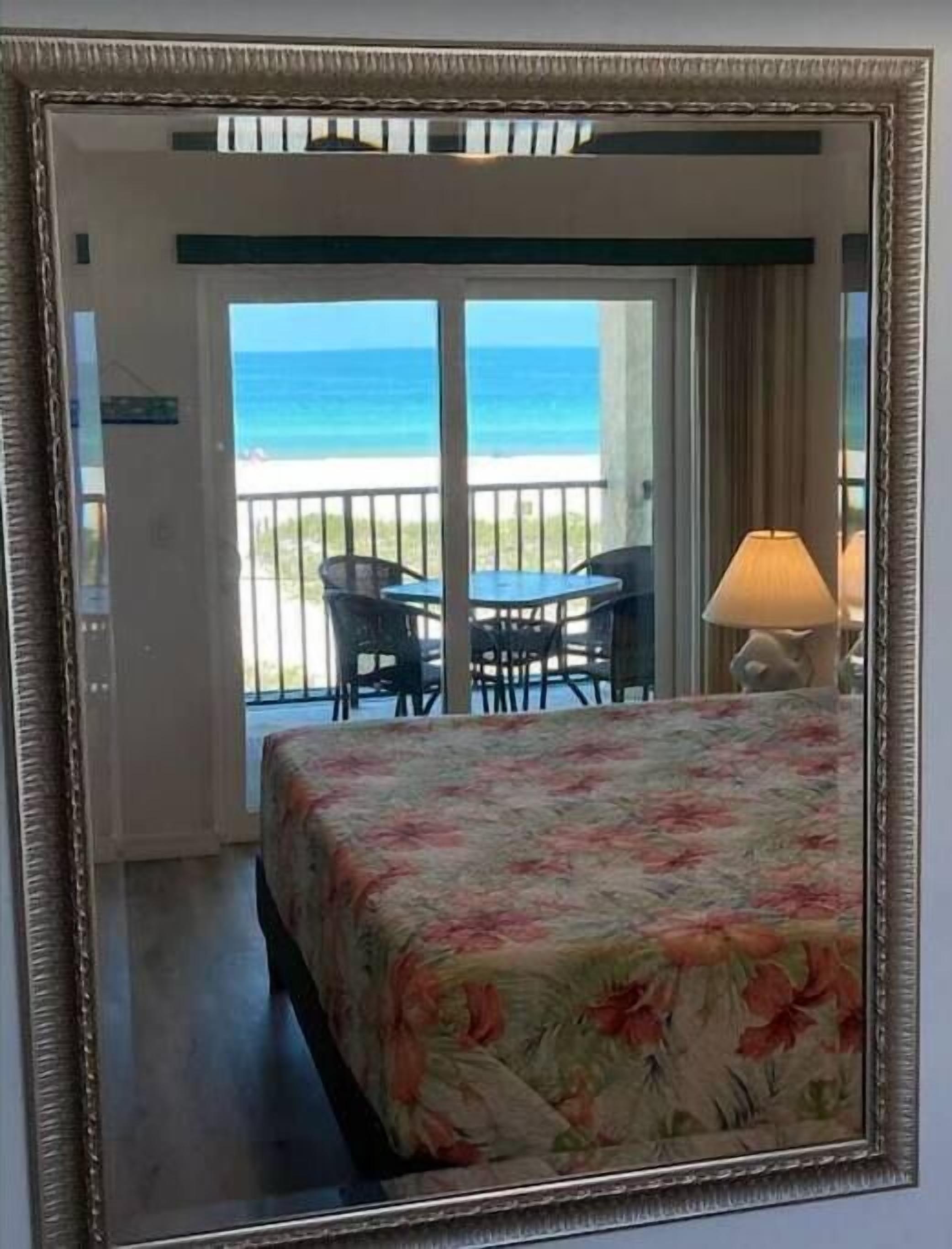 Une chambre d’hôtel avec un lit, une table et des chaises, un balcon donnant sur l’océan et une lampe.