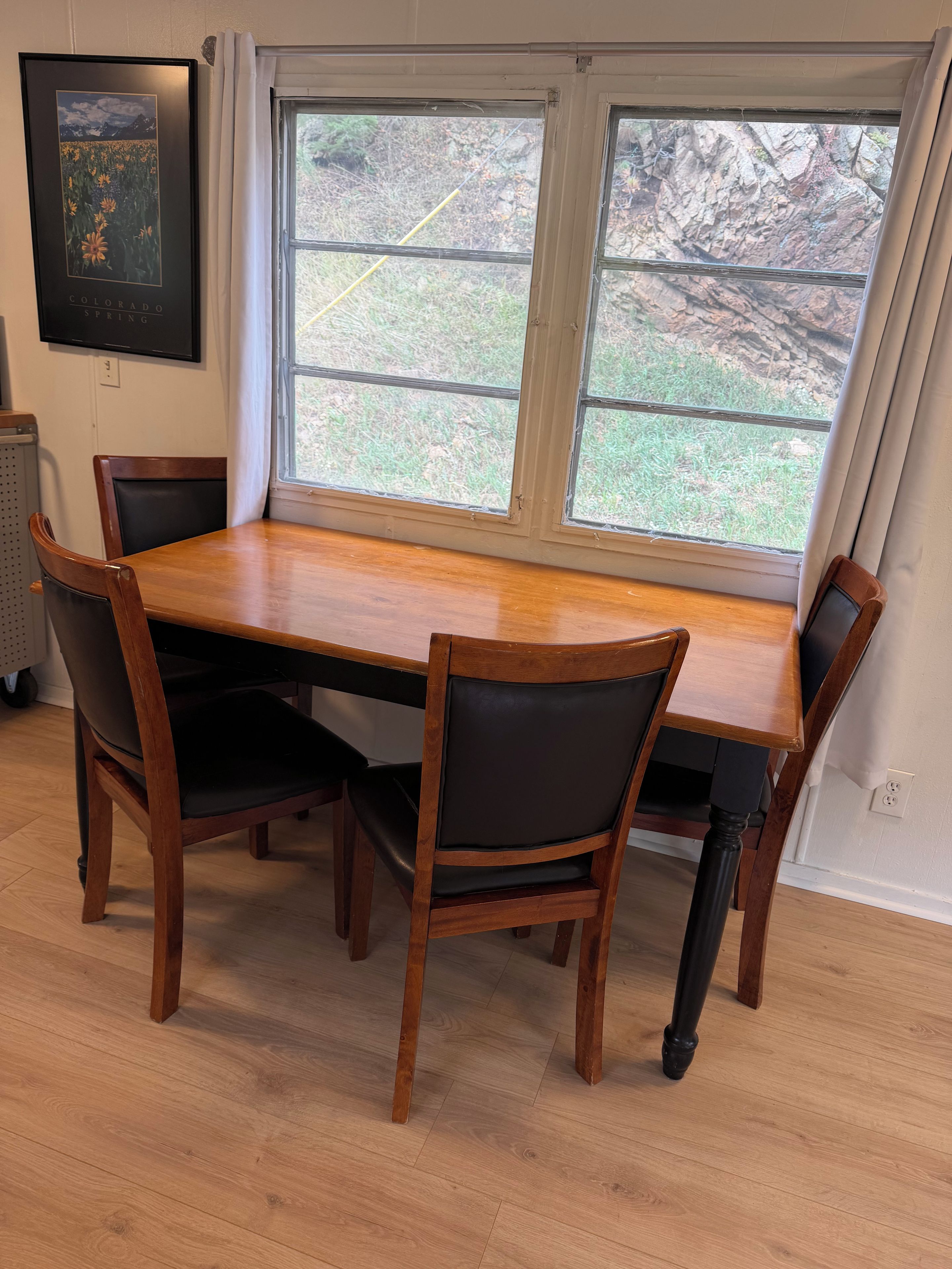 Une table à manger avec quatre chaises, une fenêtre avec des rideaux et un tableau encadré au mur.