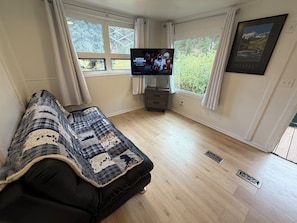 A living room with a black sofa, a flat-screen TV, a window with curtains, and a framed picture on the wall.