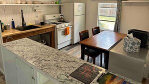 Una cocina compacta con encimera de granito, estufa, refrigerador y una mesa de comedor con sillas.