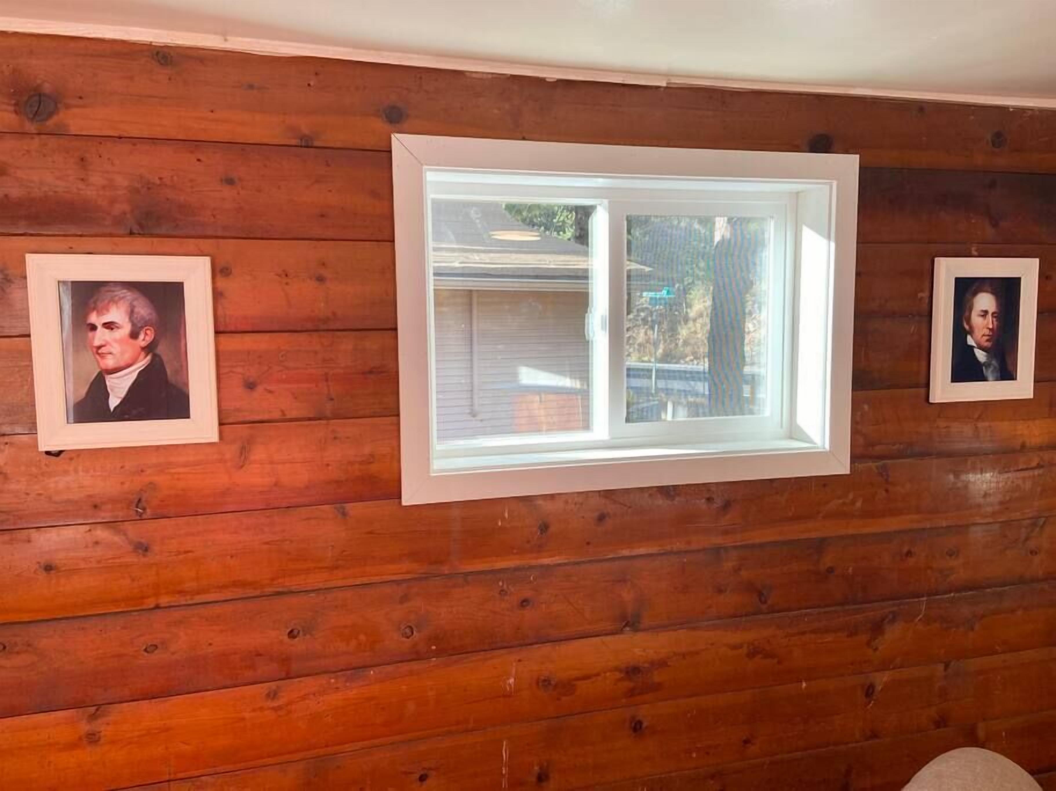 A room with wooden paneling, a large window, and two framed portraits on the wall.