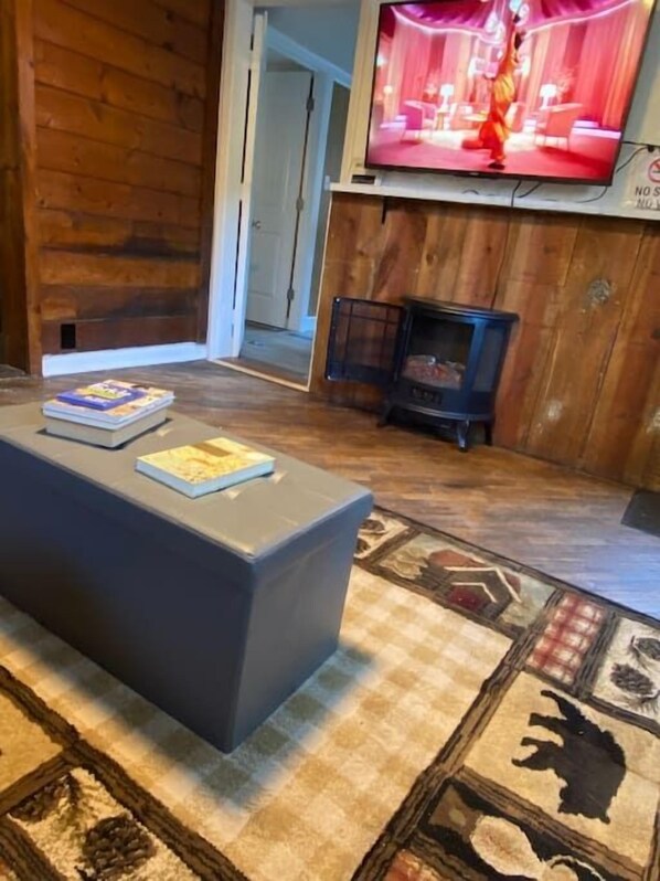 Una sala de estar con un sofá moderno, un televisor de pantalla plana montado en una pared de madera, una chimenea y un tapete estampado.