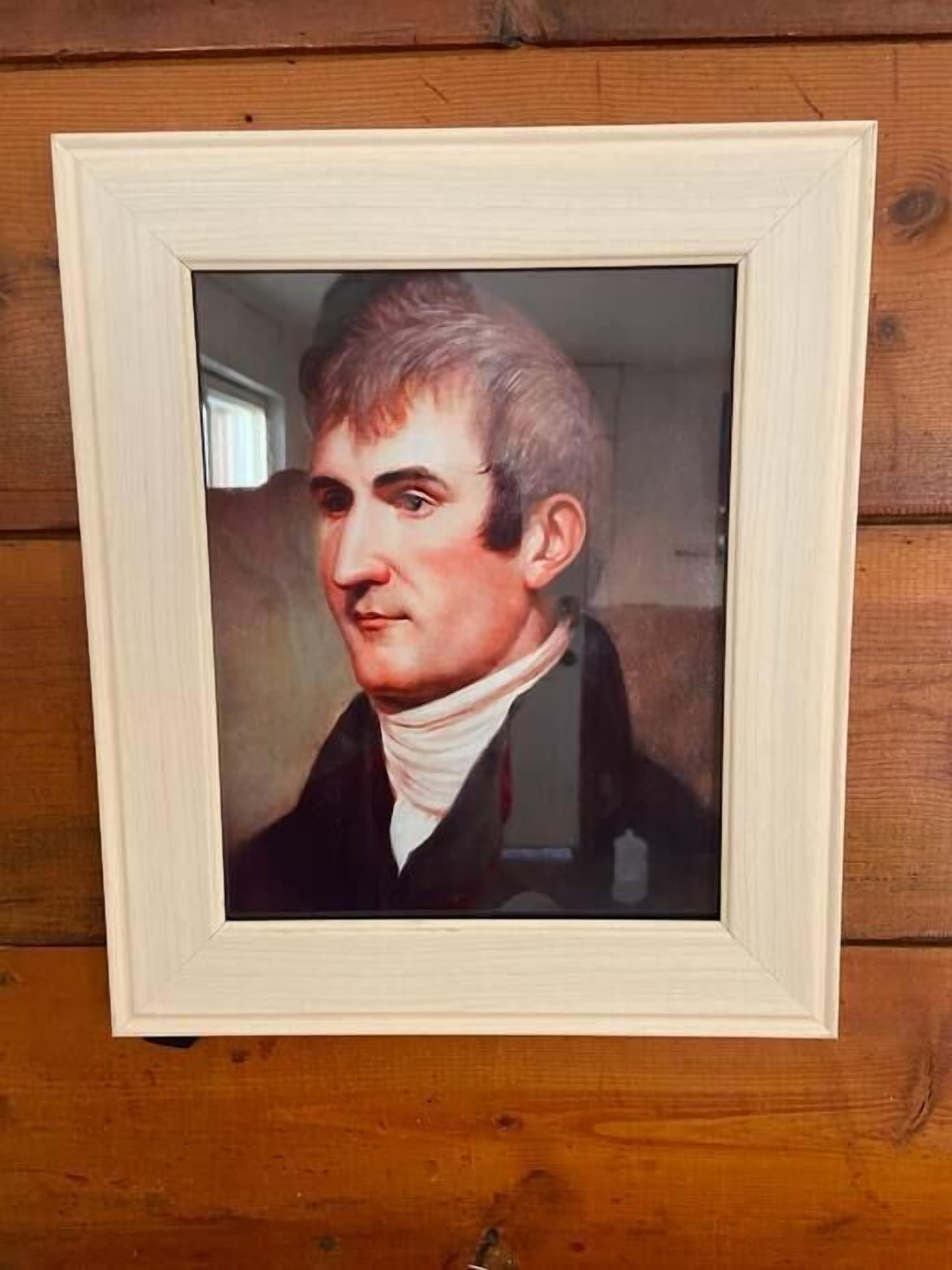 A framed portrait of a person with a white turtleneck, set against a wooden background.