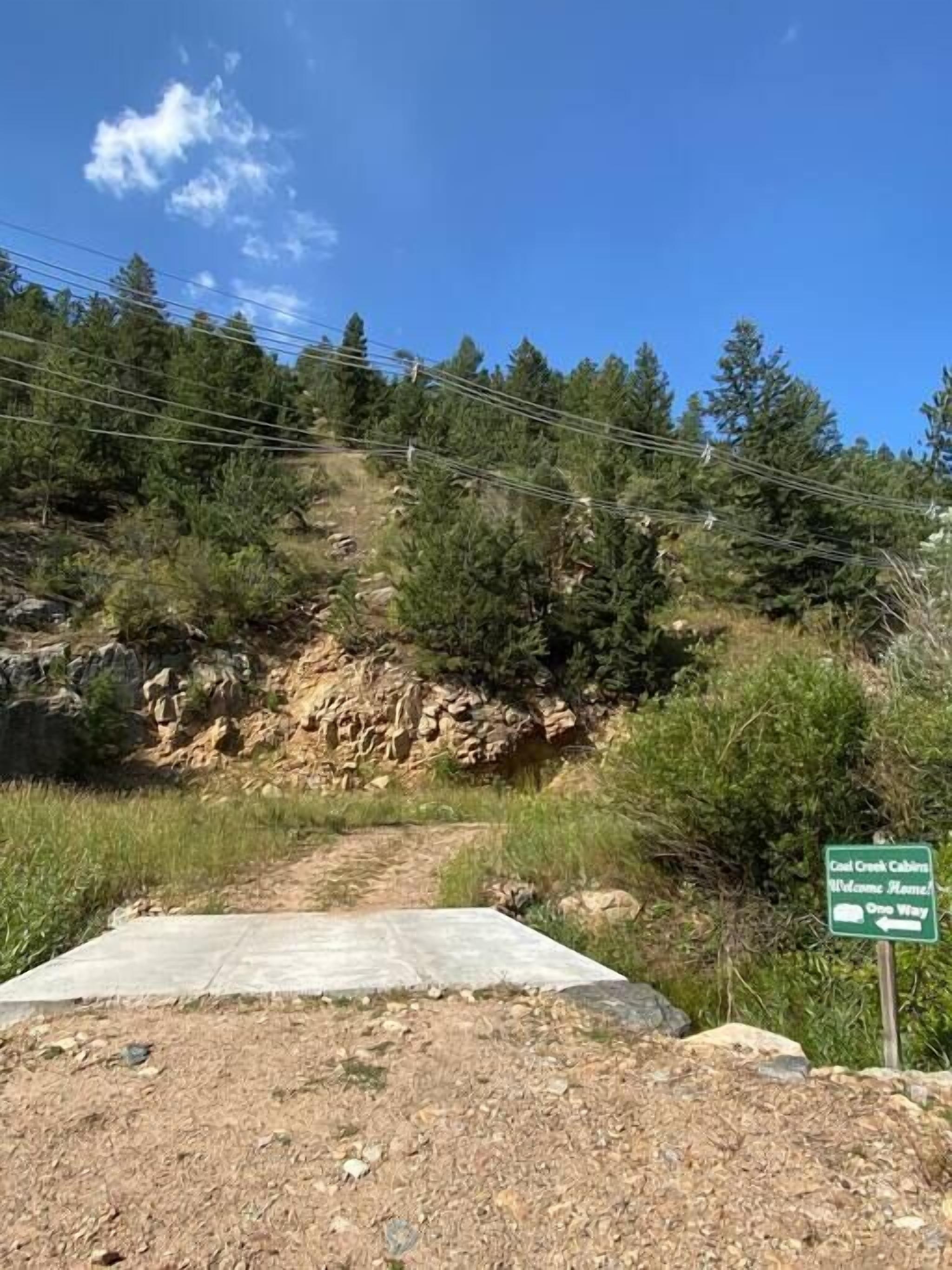 A dirt path leading uphill with a green sign indicating 'Coastal Creek Cabins Welcome Home One Way'.