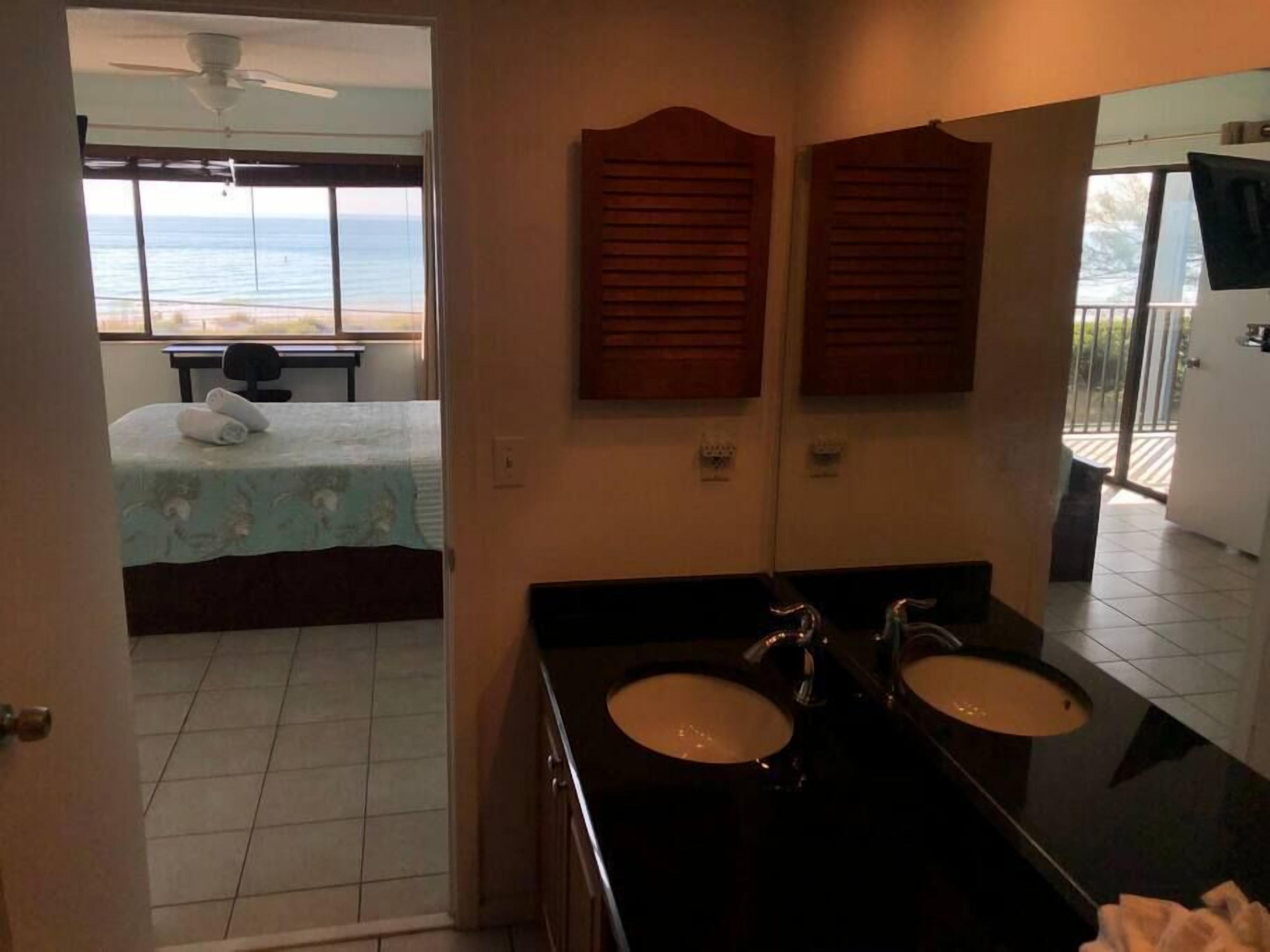 Ein Hotelzimmer mit Bett, zwei Waschbecken, Deckenventilator und Blick auf den Strand.