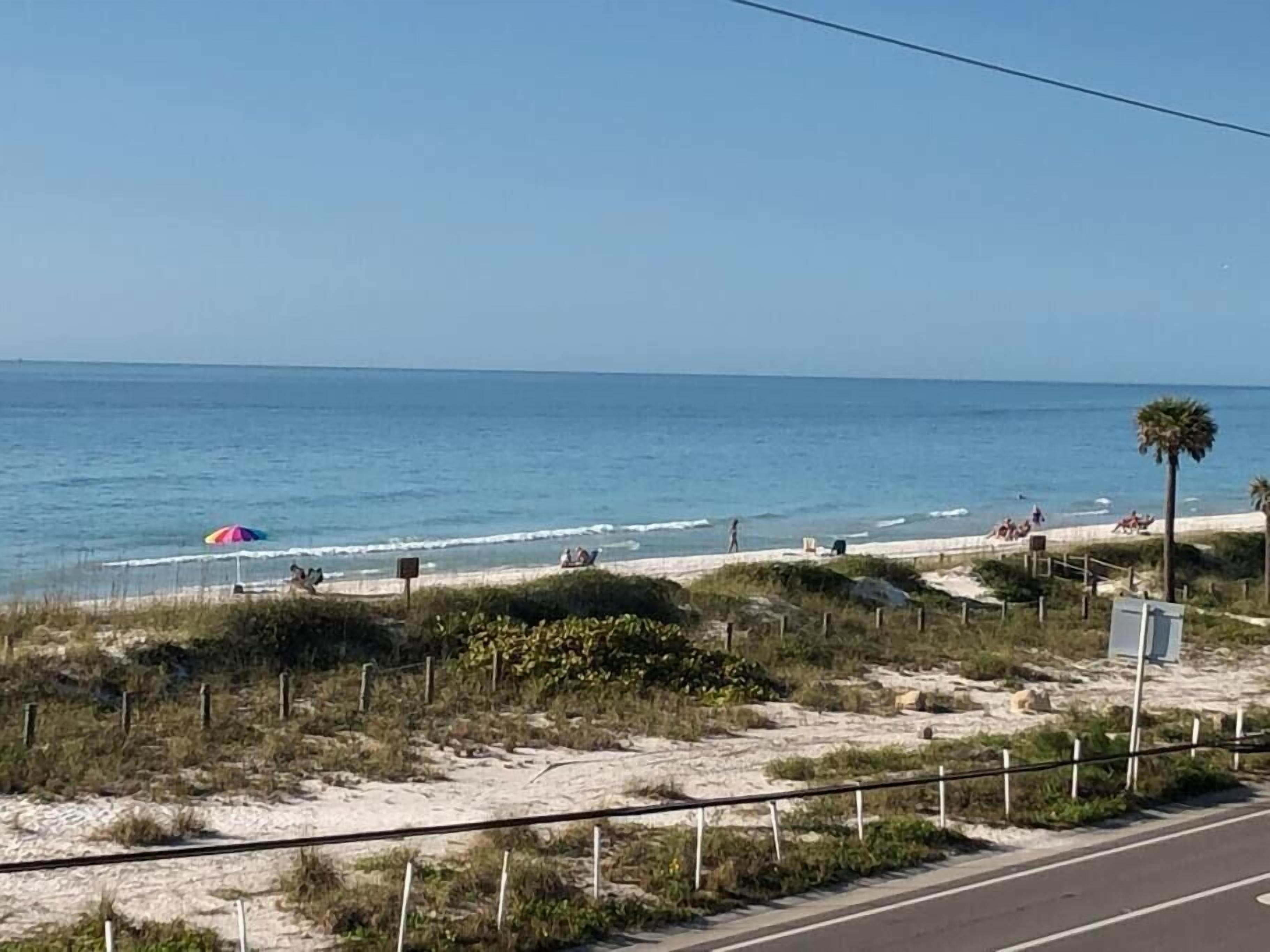 Une plage avec une clôture, des palmiers et une route.