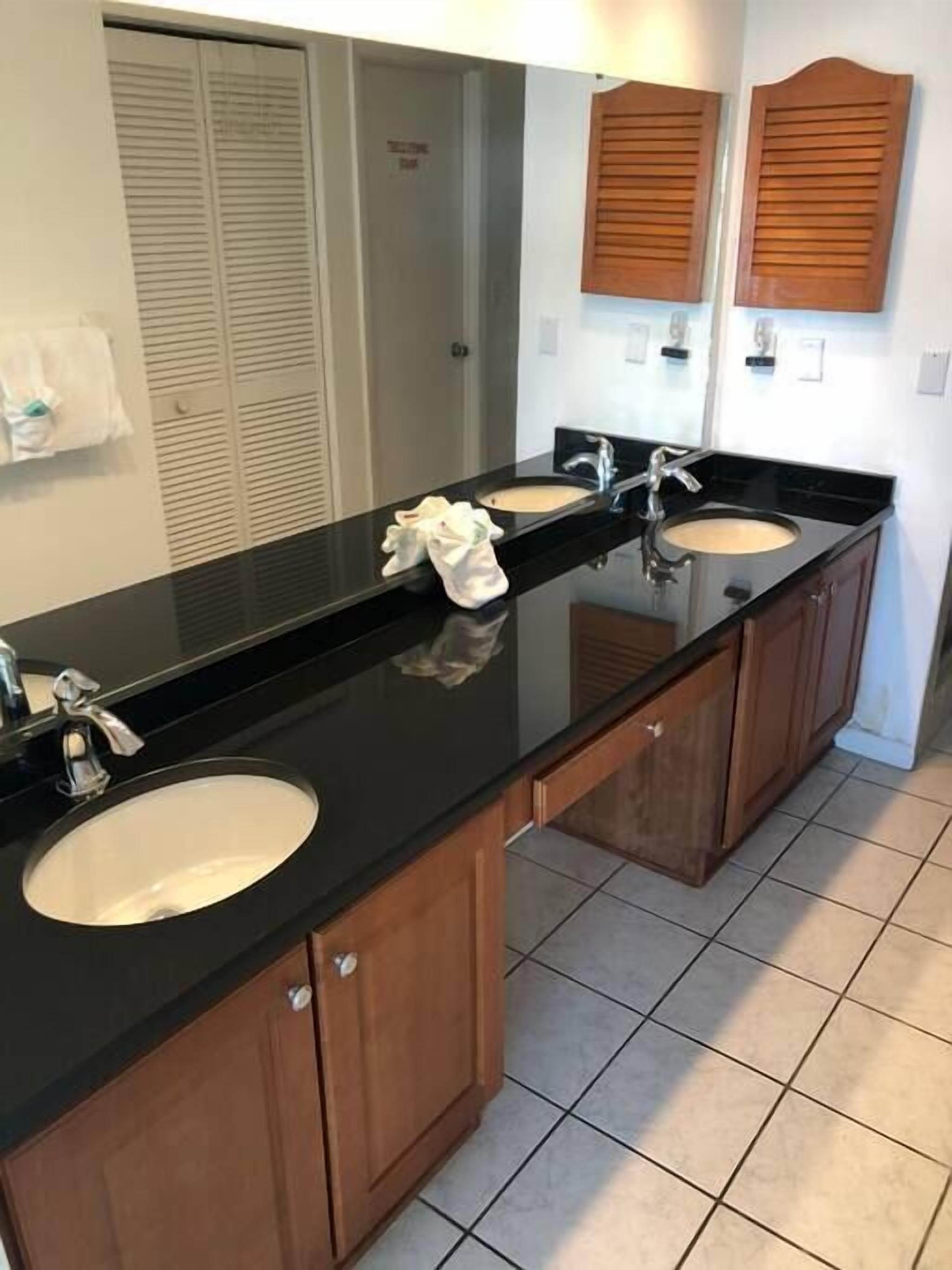 Un bagno con un piano d'appoggio nero, due lavandini, armadietti in legno, uno specchio e un portasciugamani.
