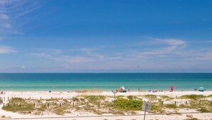A beach with a clear sky, sandy shore, and a few people and umbrellas. - AMI Beach + Gulf View Retreat - Dog-friendly (Bradenton Beach)