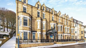 A row of traditional brick townhouses with bay windows and a central entrance with a glass canopy. - The Landings Apartment 6 (Filey)