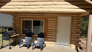 A log cabin with a patio area featuring two Adirondack chairs, a grill, and a sliding glass door. - Piedra River Outpost (Bayfield)