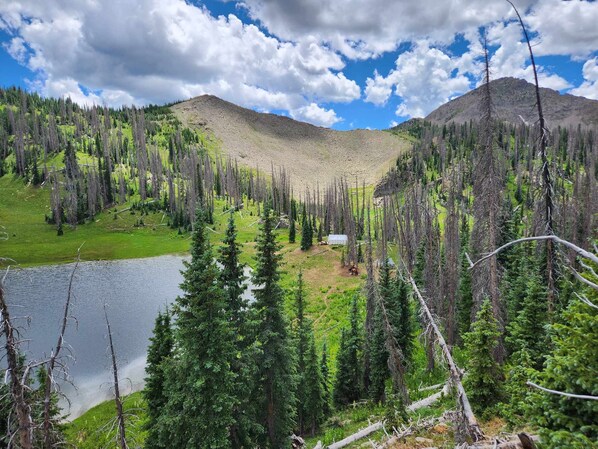 A mountainous landscape with a lake, dense forest, and a small cabin. - Piedra River Outpost (Bayfield)
