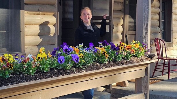 A person standing on a porch with a flower bed in front. - Piedra River Outpost (Bayfield)