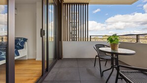Un balcón con puerta de cristal, una pequeña mesa con sillas y una planta en maceta.