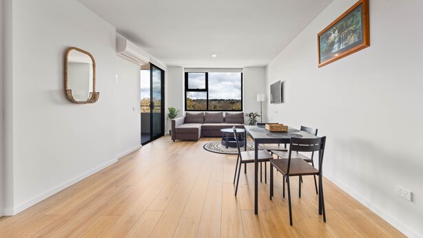 Una sala de estar moderna con sofá, mesa de comedor y sillas. Una ventana grande ofrece vistas al exterior.