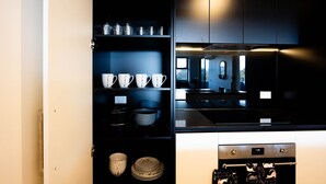 Cocina moderna con gabinetes negros, electrodomésticos de acero inoxidable y un vidrio que muestra vajilla y utensilios de cocina ordenados.