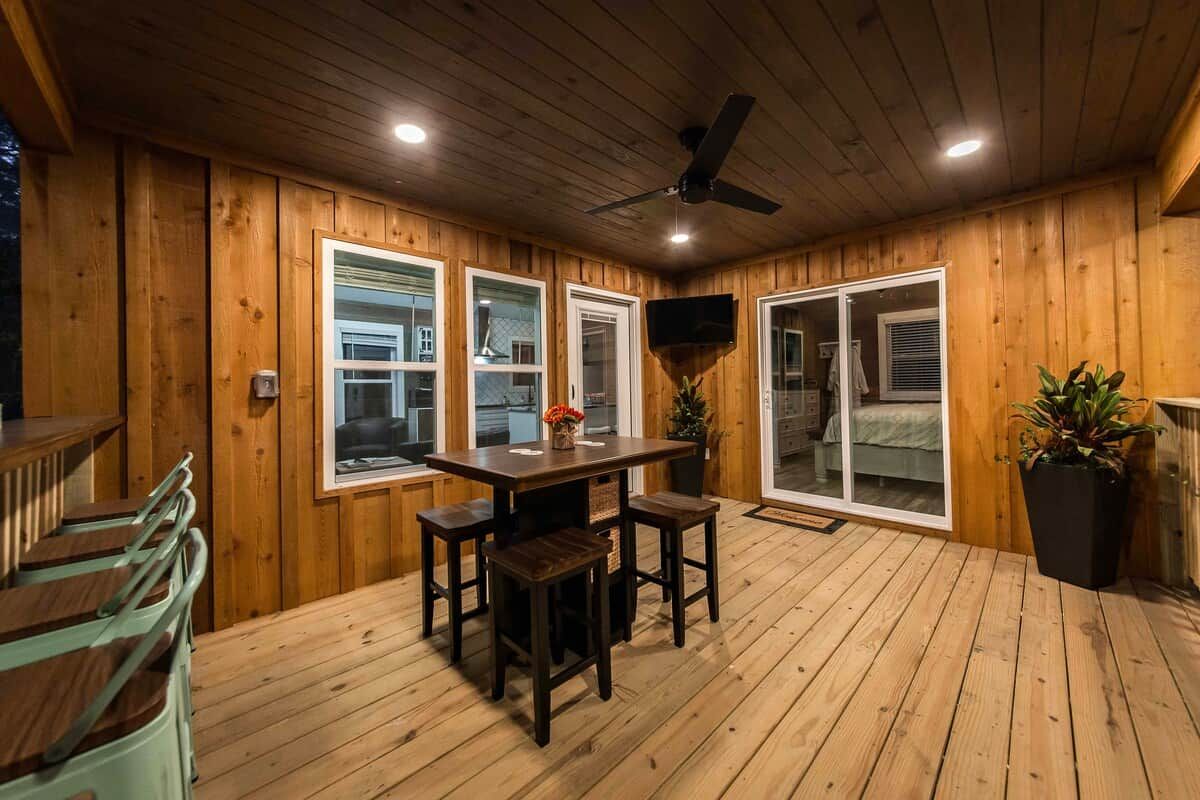 Habitación con piso de madera, una mesa, sillas, ventilador de techo y puerta corrediza de vidrio que da a un dormitorio.