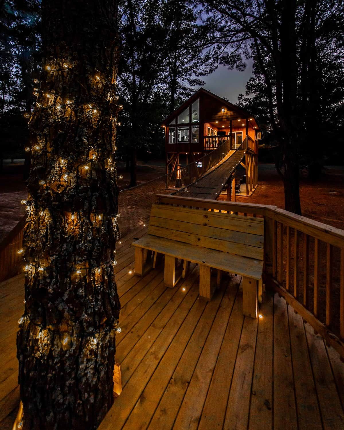 Una terraza de madera con un banco, una escalera que lleva a un edificio y un árbol con luces.