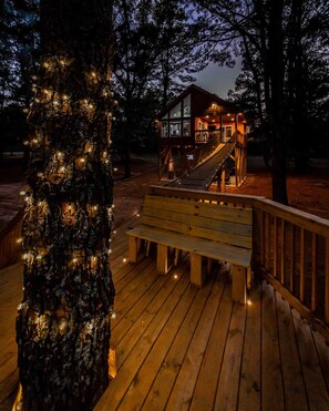 A wooden deck with a bench, a staircase leading to a building, and a tree with lights.