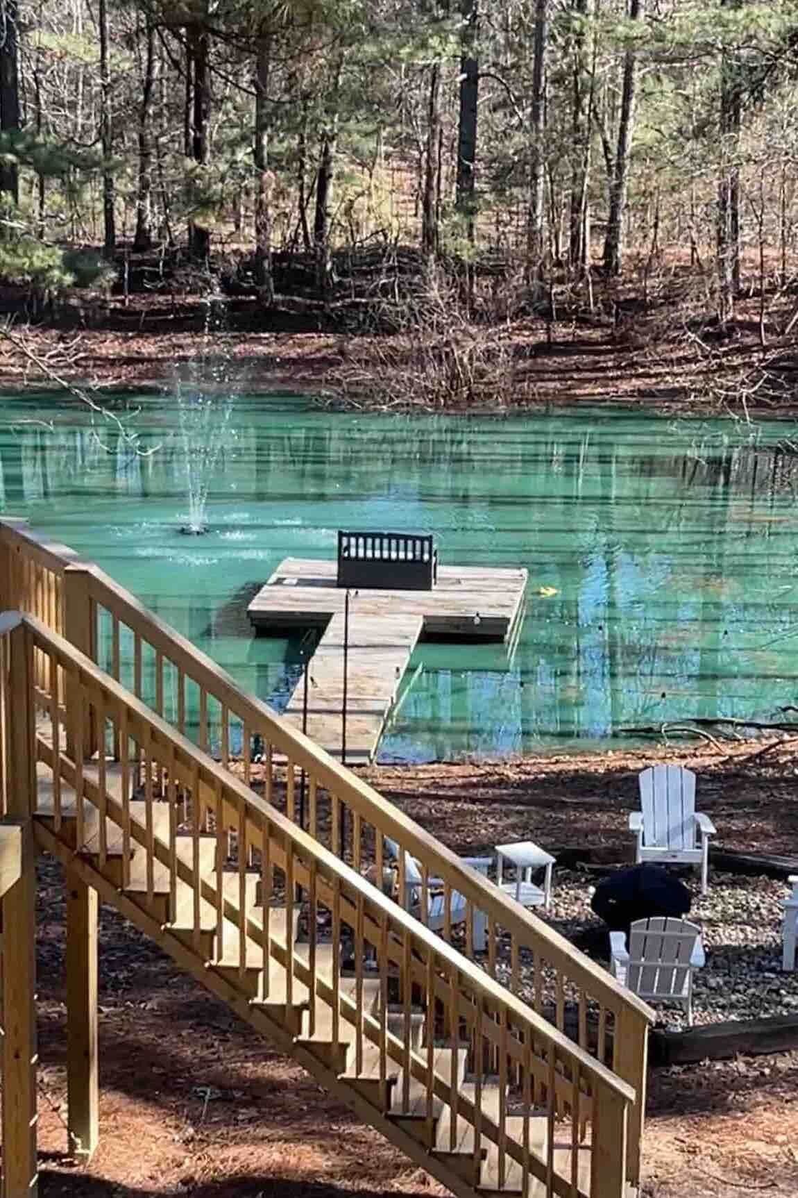 Un escalier en bois mène à une jetée surplombant une étendue d’eau claire, le tout étant entouré d’arbres.