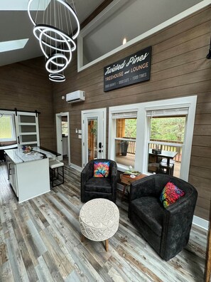 Moderni sisustus, jossa on kyltti, jossa lukee ”Twisted Pines Treehouse and Lounge”. Tiloissa on keittiöalue, värikkäillä tyynyillä varustettu oleskelualue ja suuret ikkunat.
