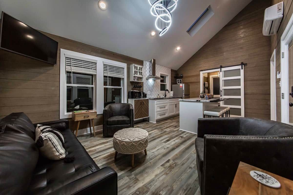 A modern living room with a sofa, ottoman, and a dining area with a table and chairs.
