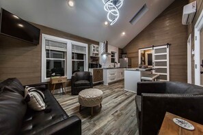 A modern living room with a sofa, ottoman, and a dining area with a table and chairs.