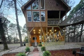 A wooden cabin with a balcony, surrounded by trees.