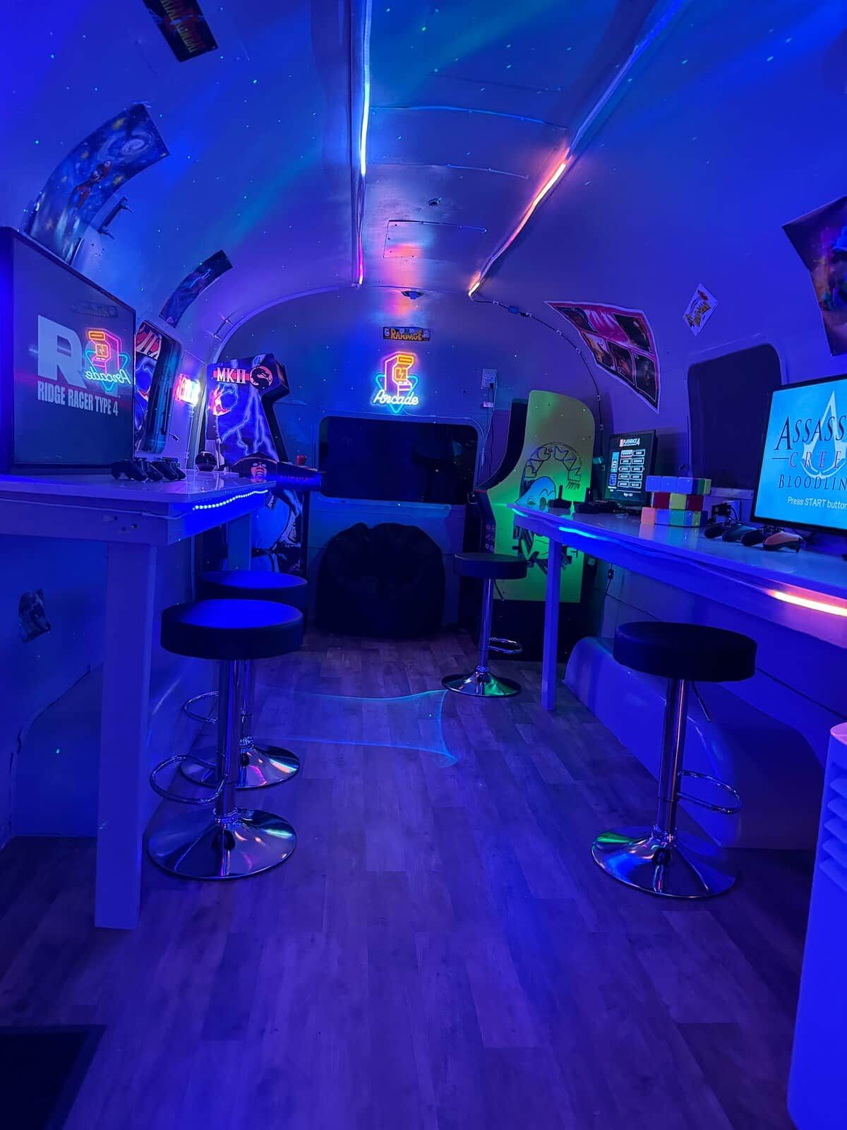 A bar area with neon signs, arcade machines, and a monitor displaying a game.