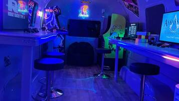 A bar area with neon signs, arcade machines, and a monitor displaying a game.