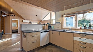 A modern kitchen with wooden cabinets, a dishwasher, and a large window.