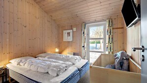 A wooden-paneled bedroom with a bed, a bedside table, a TV, and a window with curtains.