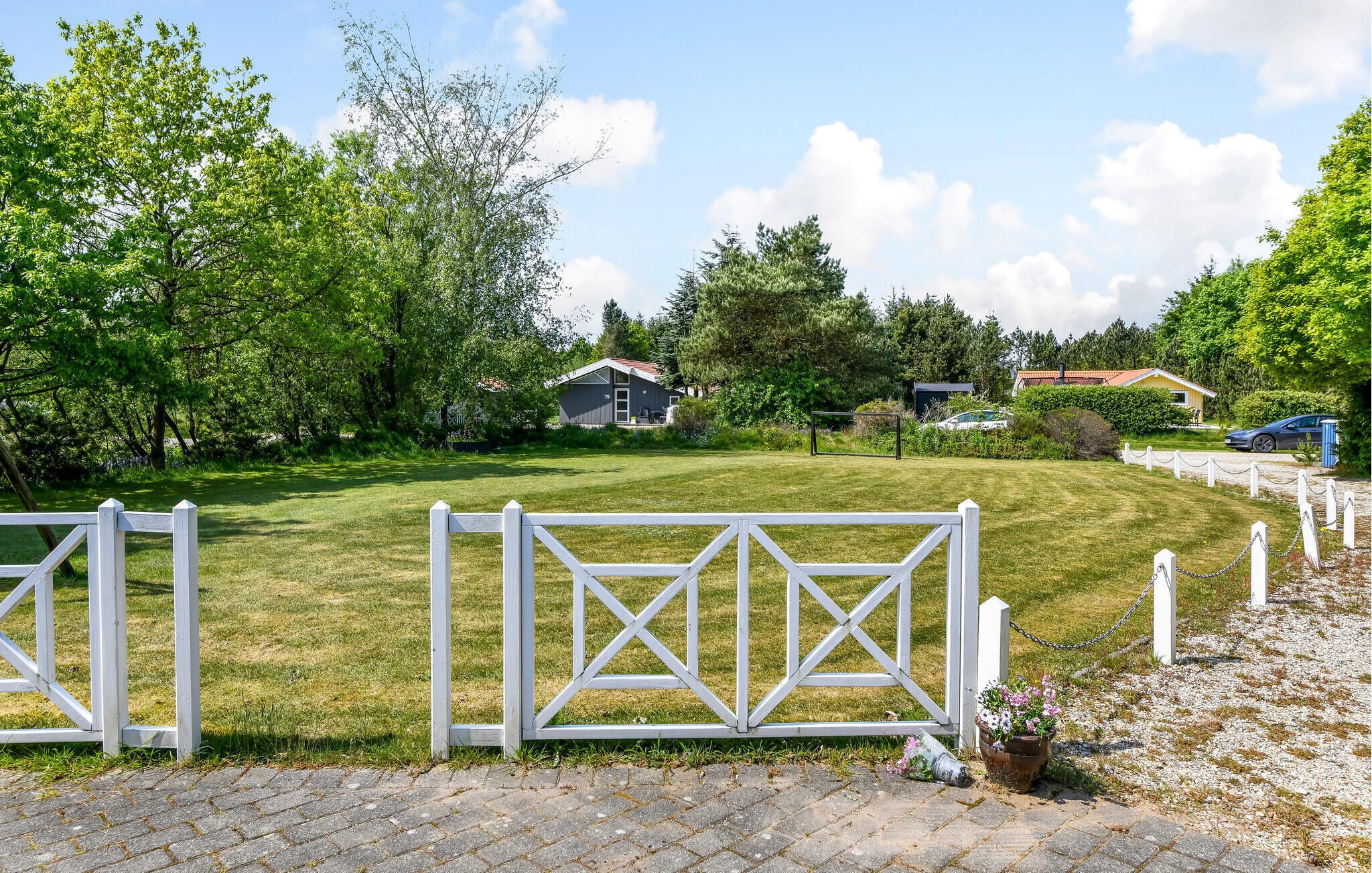 Une propriété clôturée avec une pelouse verdoyante, un petit bâtiment et un chemin piétonnier dallé.