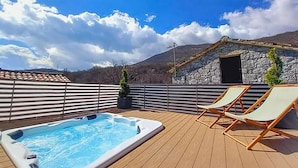 A wooden deck with a hot tub and lounge chairs, a stone building, and a mountainous backdrop. - Gorgeous home in Veprinac (Veprinac)